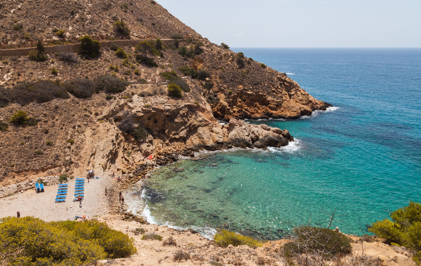A view of the secluded, rocky cove of Cala Tío Ximo surrounded by wild cliffs.