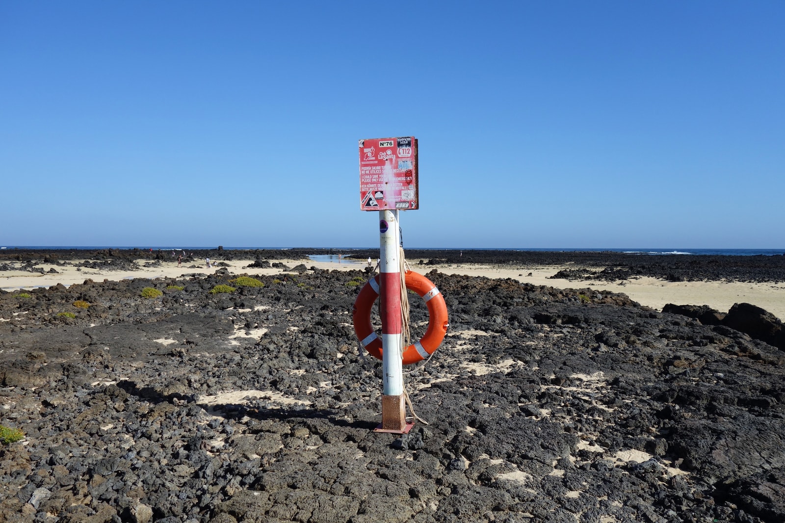 A lifebuoy and a warning sign stand on a rocky outcrop overlooking the water.