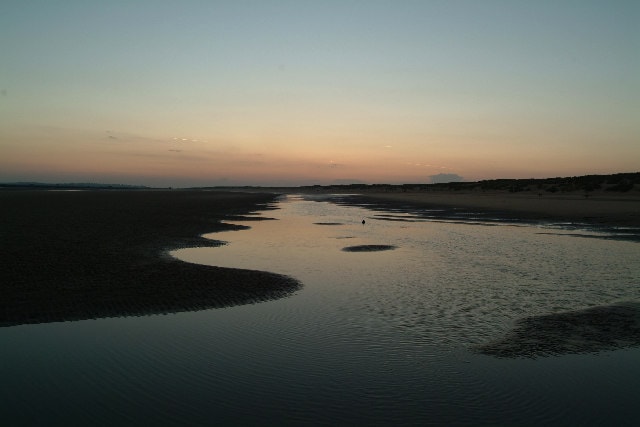 The wet sands at low tide reflect the colors of the sunset.
