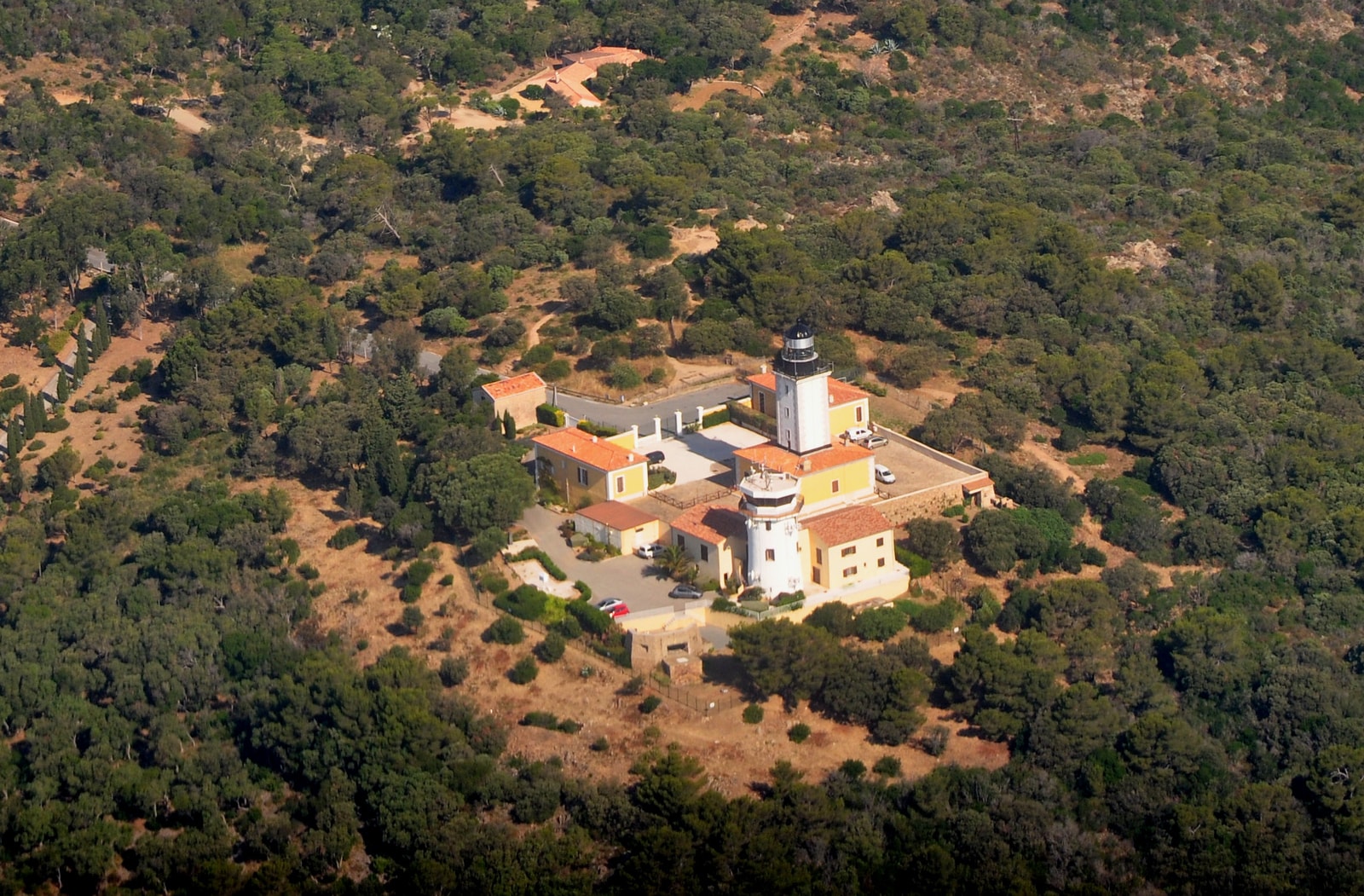 Aerial view of the rugged cliffs and dense green Mediterranean forest surrounding the Cap Camarat lighthouse.