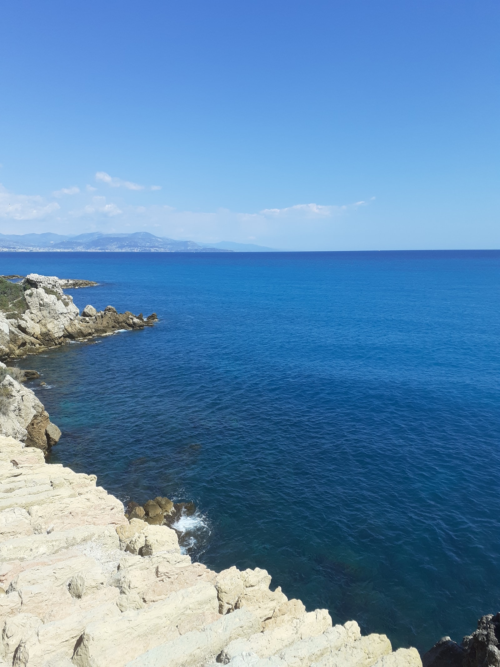 White limestone cliffs drop dramatically into the deep blue Mediterranean Sea along a rugged coastline.