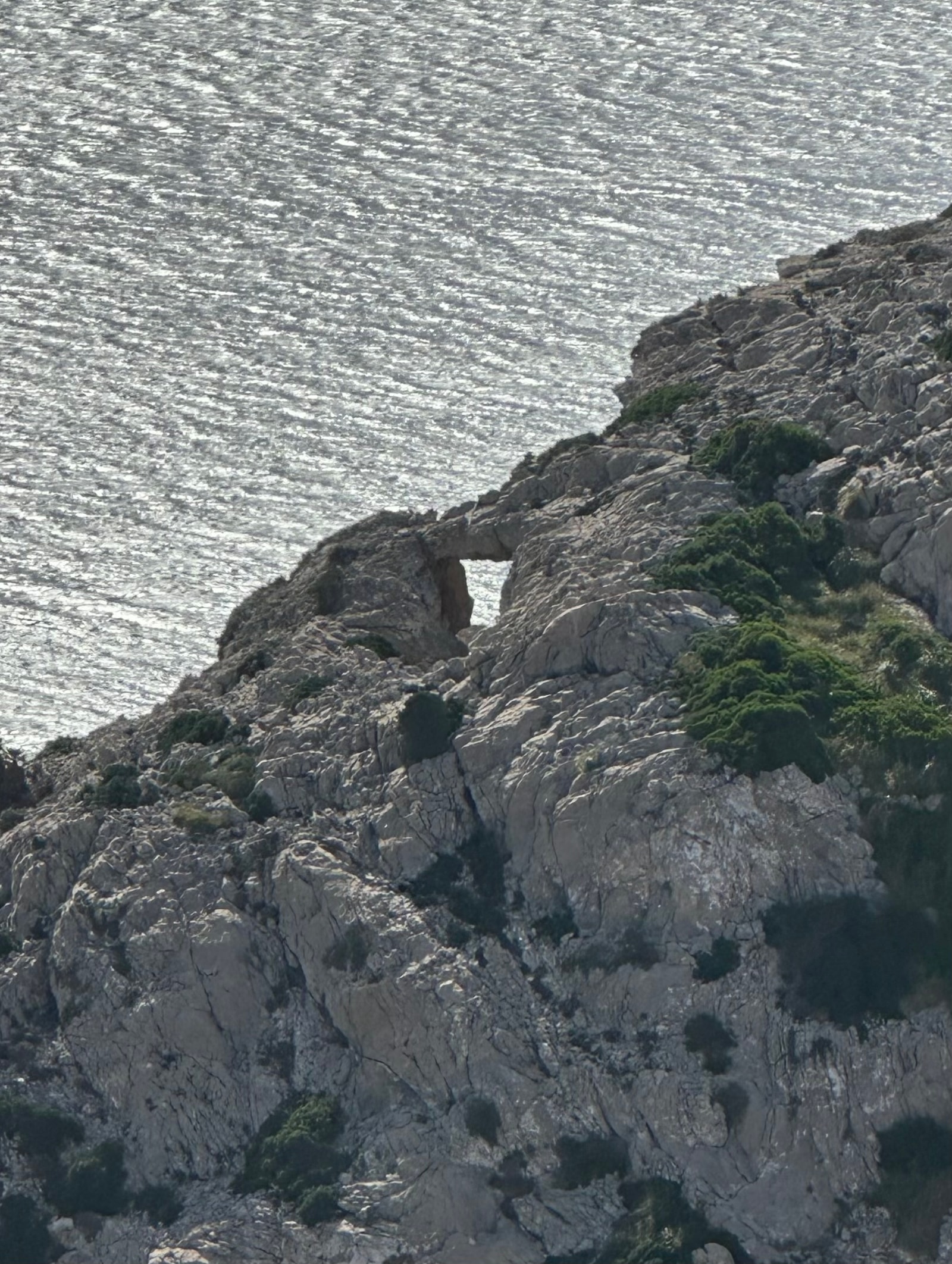 A large natural rock arch stands on a rugged, cliff-lined coast overlooking the sea.
