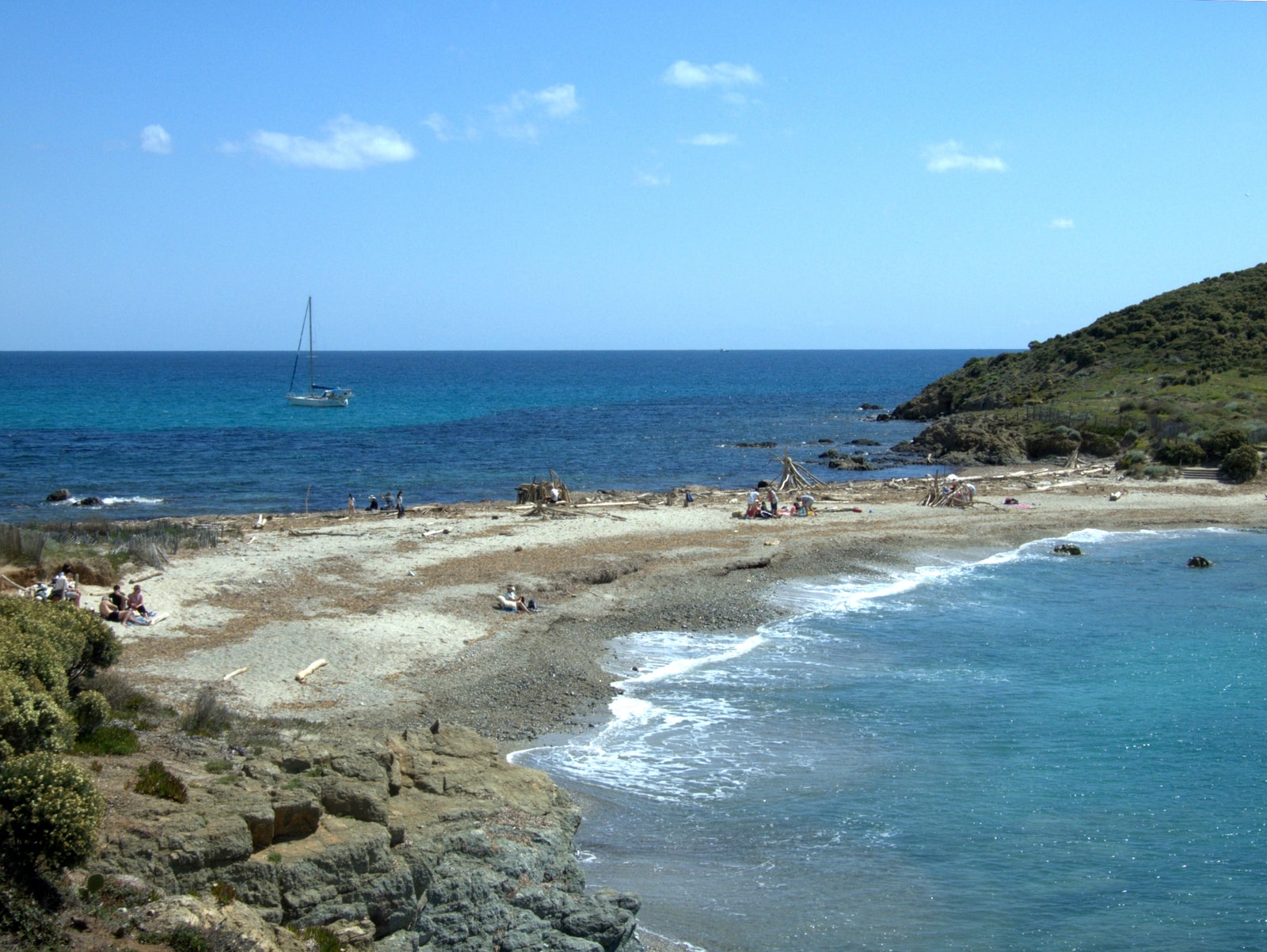 The wild sandy spit of Cap Taillat with rocky headlands and shallow, translucent waters.