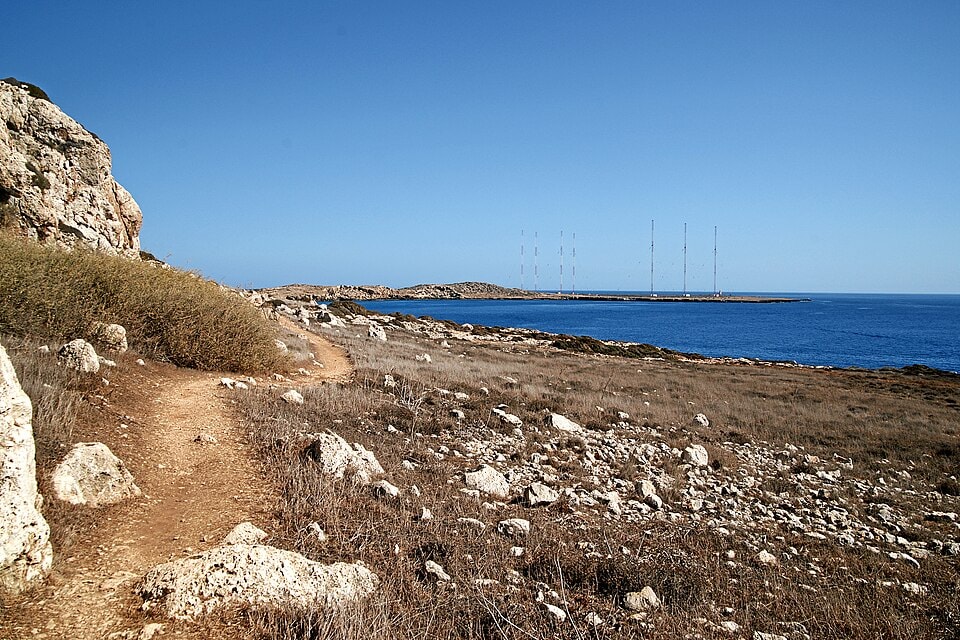 A coastal footpath winds through the dry, rocky landscape of Cape Greco under a sunny sky.