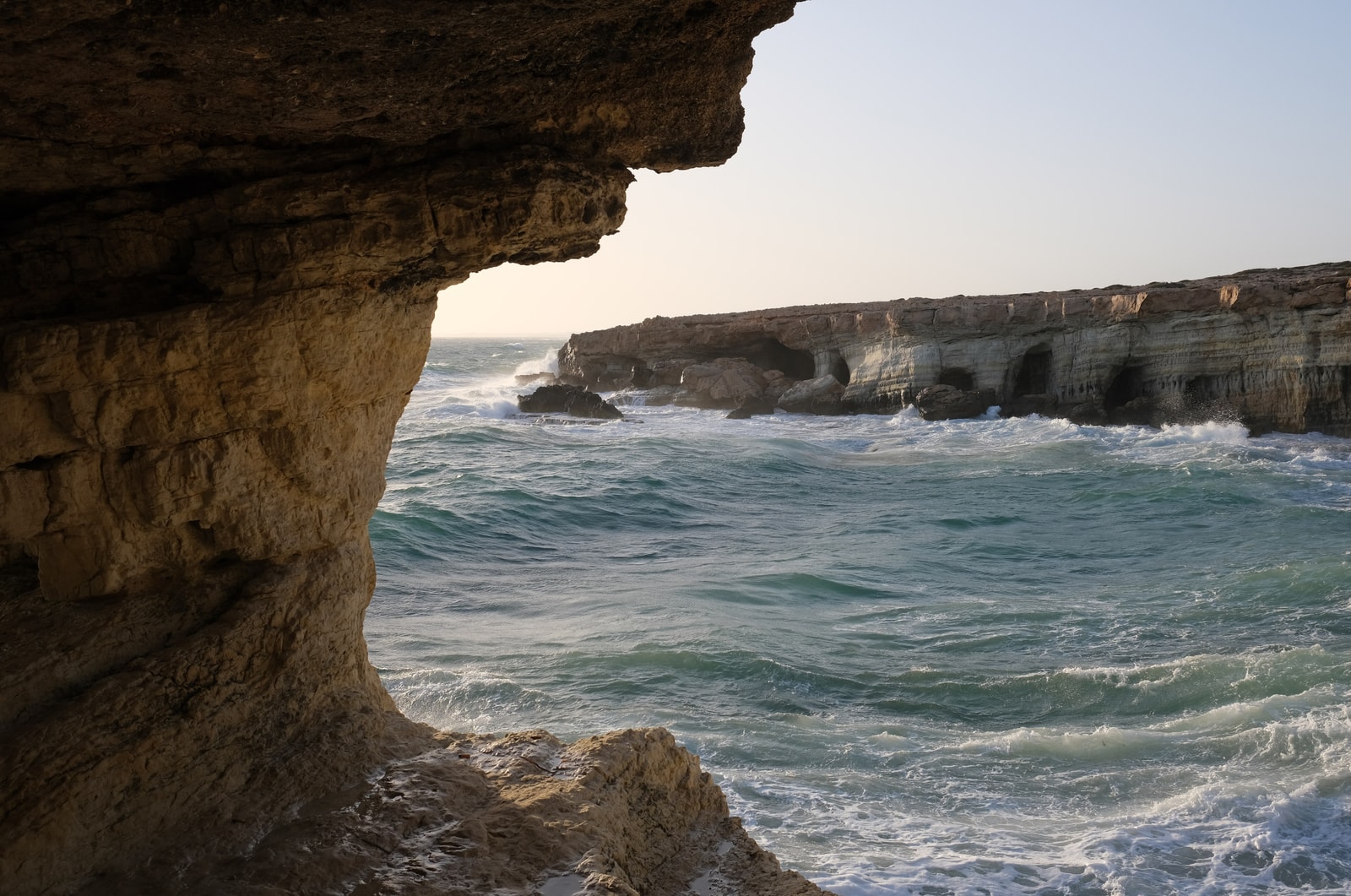 A view from inside a sea cave at Cape Greco, framing the turquoise sea and distant cliffs.