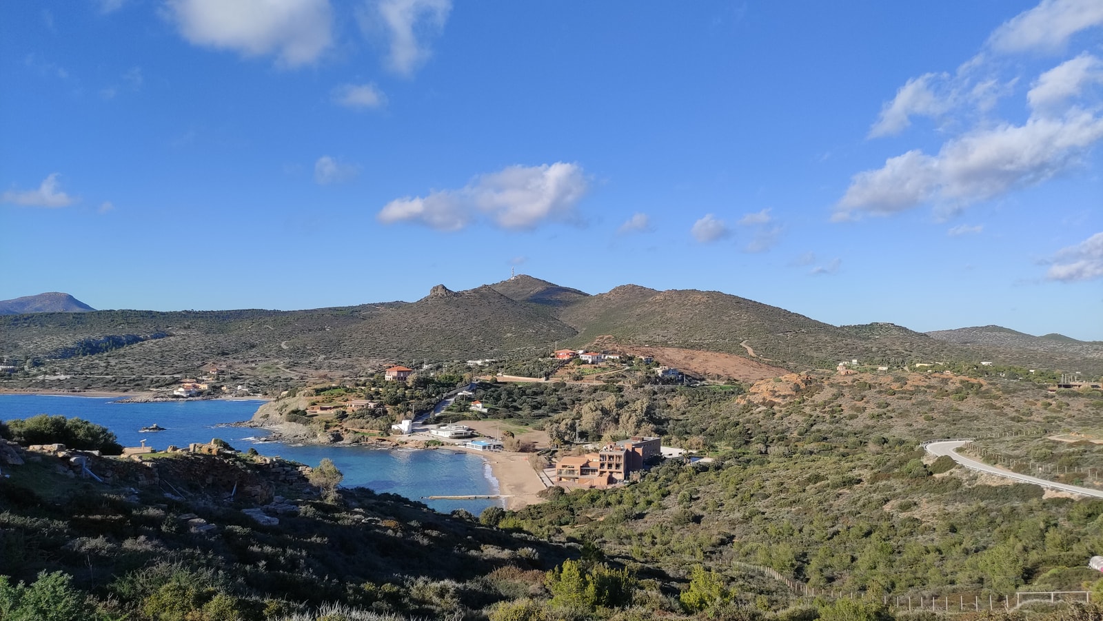 An elevated view shows a winding road along a rugged peninsula with dry hills and blue water.