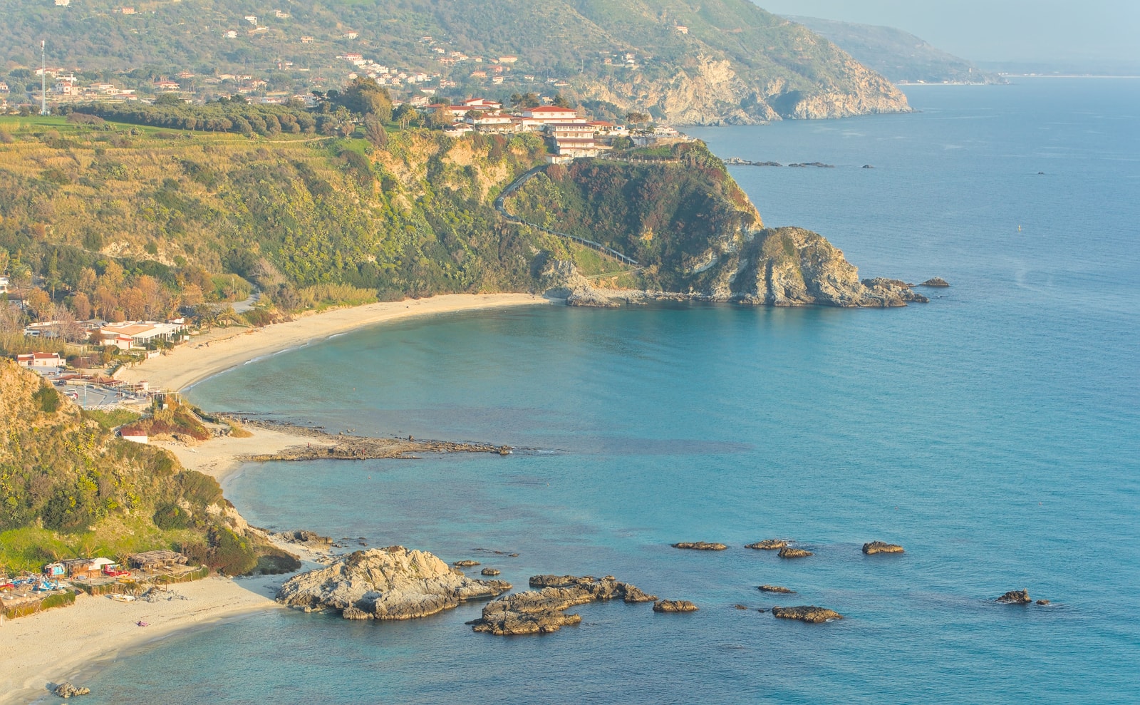 A panoramic view of the rugged, green-draped cliffs and sweeping sandy coves of Grotticelle beach at Capo Vaticano.