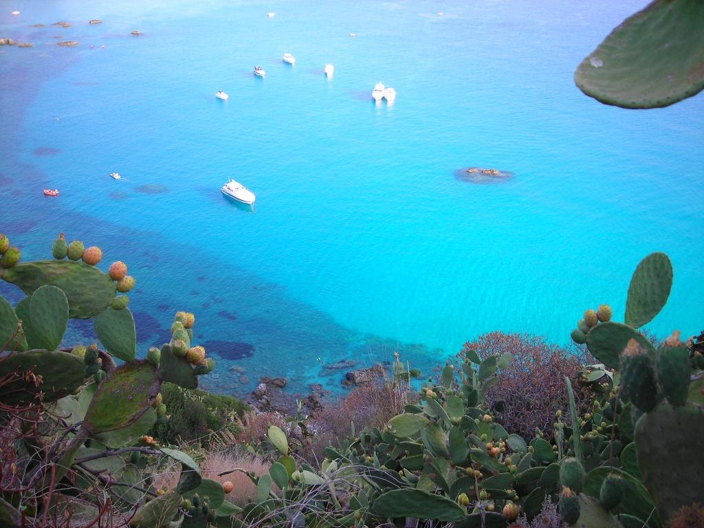 Dramatic vertical sandstone cliffs covered in green shrubs drop into the sea at Praia i Focu near Capo Vaticano.