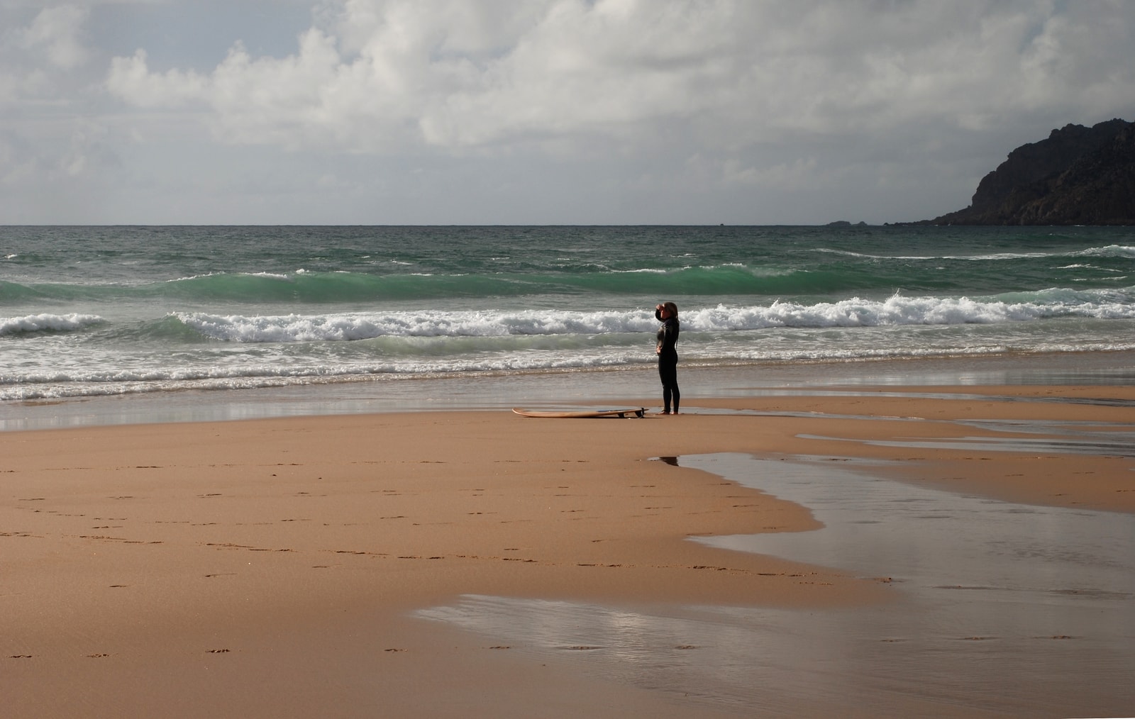 A surfer walking along the shoreline of Guincho Beach at sunset in solitary, contemplative atmosphere