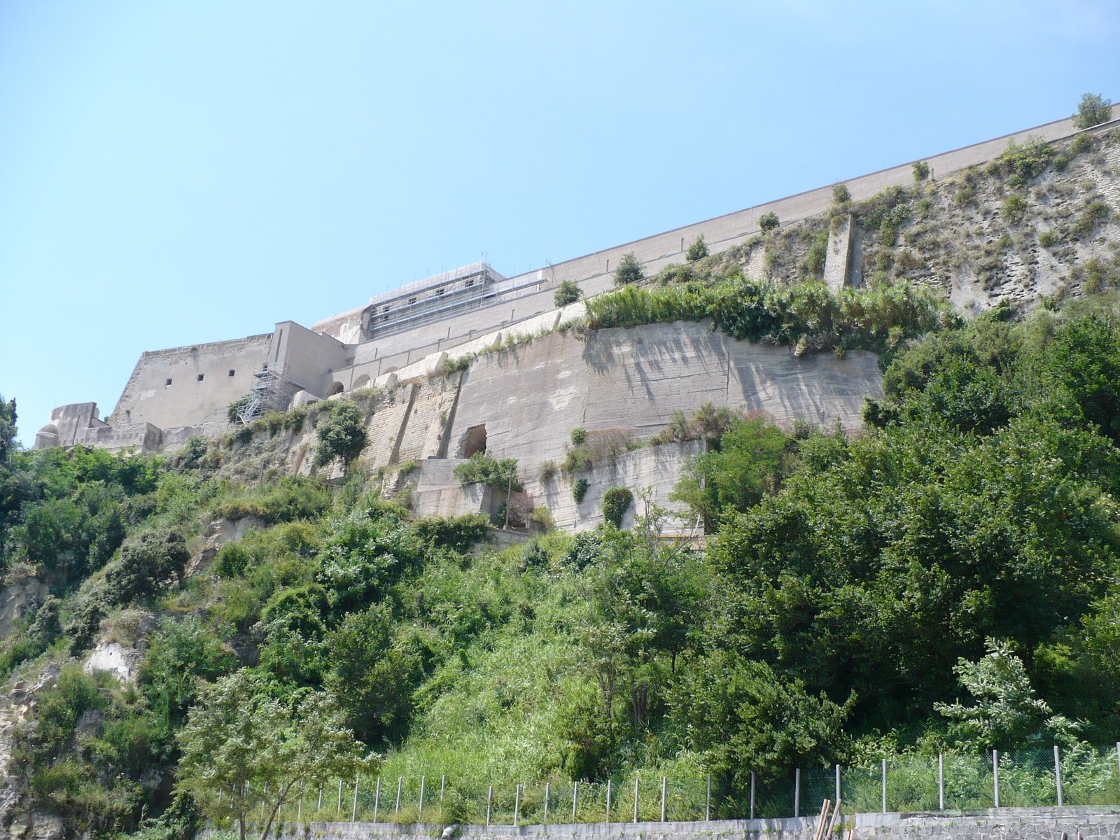 The secluded beach of Castello di Baia, with sunbeds on the sand and the massive stone walls of the Aragonese Castle rising up the cliffside directly behind it.