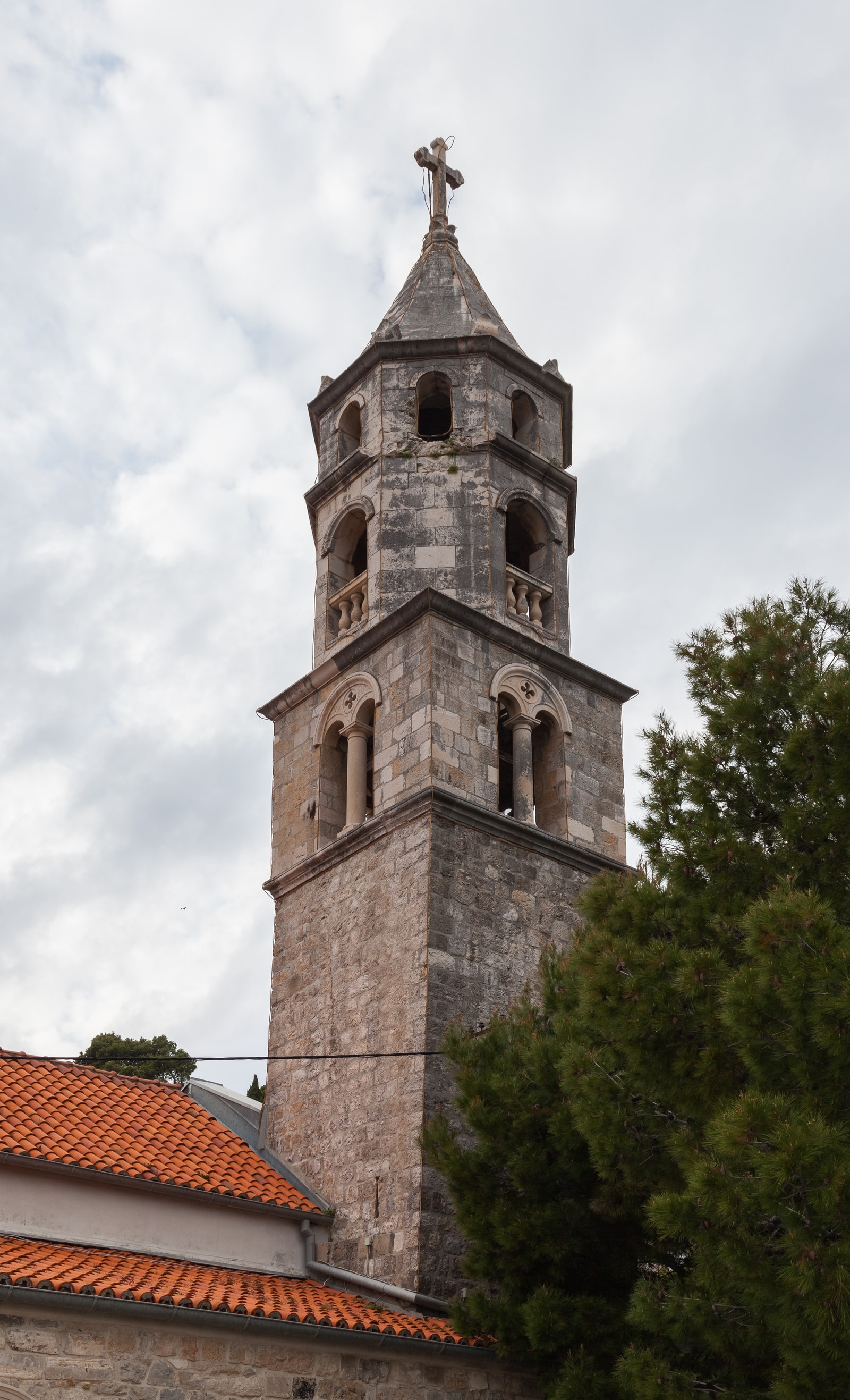 A historic stone monastery with a bell tower, located at the tip of a peninsula with the sea in the background.