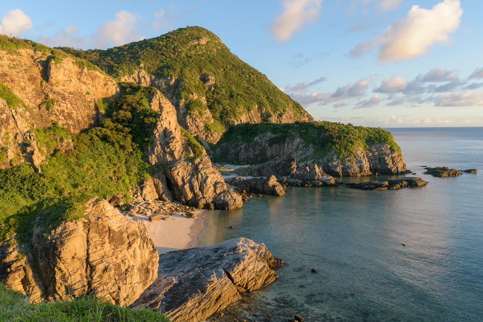 A view of steep, green cliffs meeting a deep blue sea under a partly cloudy sky.