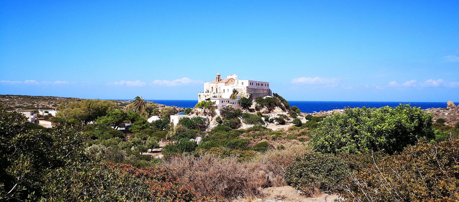 A panoramic shot of the white-washed Chrysoskalitissa Monastery against a bright blue sky.