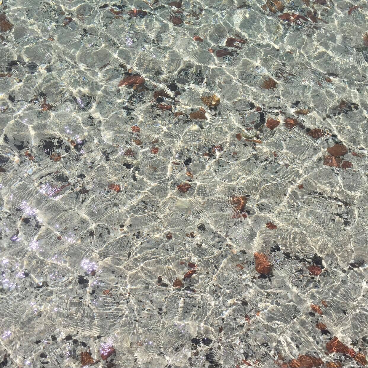 A clear, square-format shot of transparent, shallow water over a sandy bottom.
