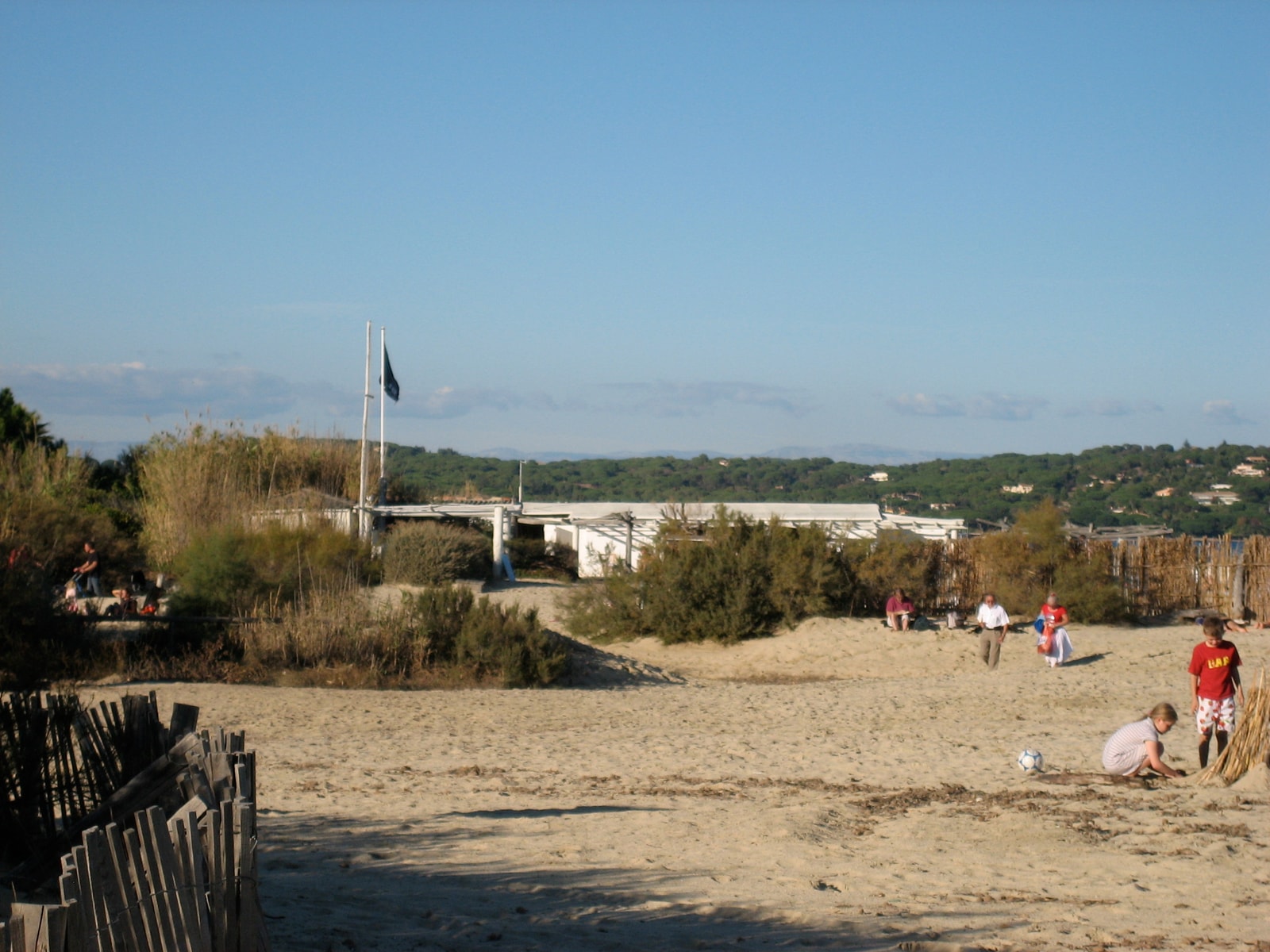 The rustic wooden entrance and fence of the iconic Club 55, set against the sand dunes of Pampelonne Beach.