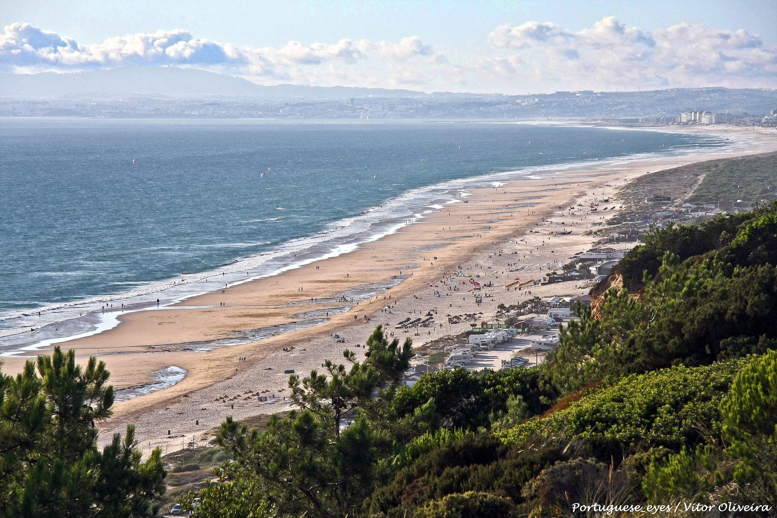 The expansive golden shoreline of Fonte da Telha under towering fossil cliffs along Costa da Caparica