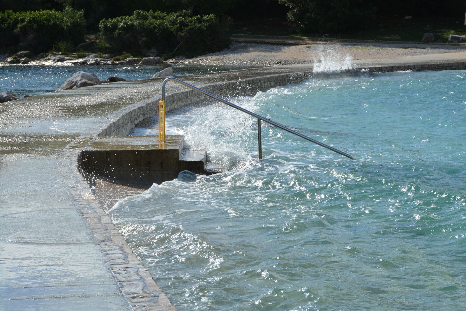 A concrete causeway connects the islets of Sveti Andrija and Maškin, with turquoise waves splashing against the sides.