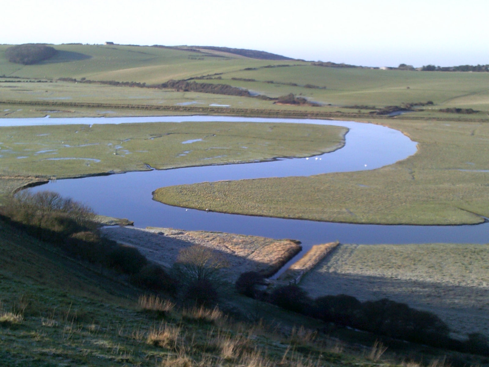 An elevated view of the Cuckmere River's winding S-shaped meanders as it flows through flat marshland towards the sea.