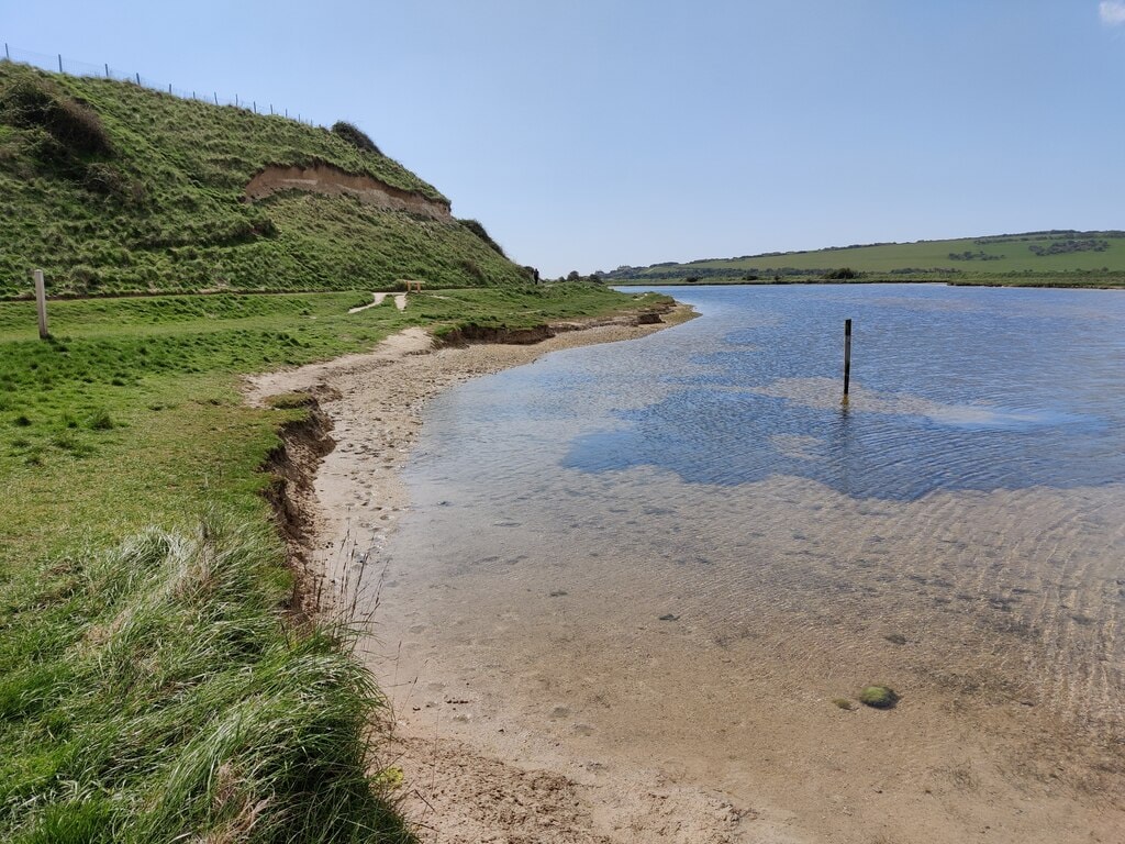 The Cuckmere River winds through grassy salt marshes within the Seven Sisters Country Park under a cloudy sky.