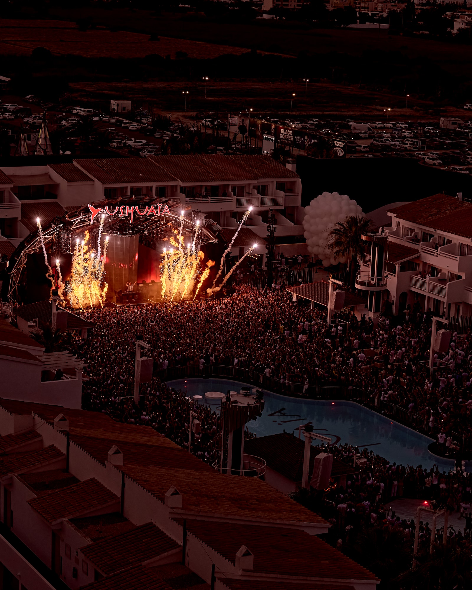 A massive crowd fills the poolside area at Ushuaïa Ibiza during a night event with dramatic stage lighting and pyrotechnics.