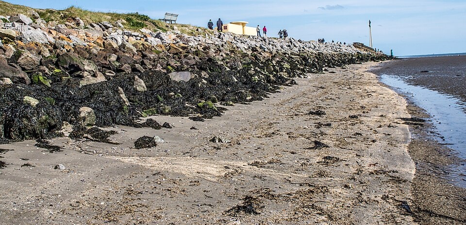A rocky shore with green algae is visible at low tide on a wide beach.