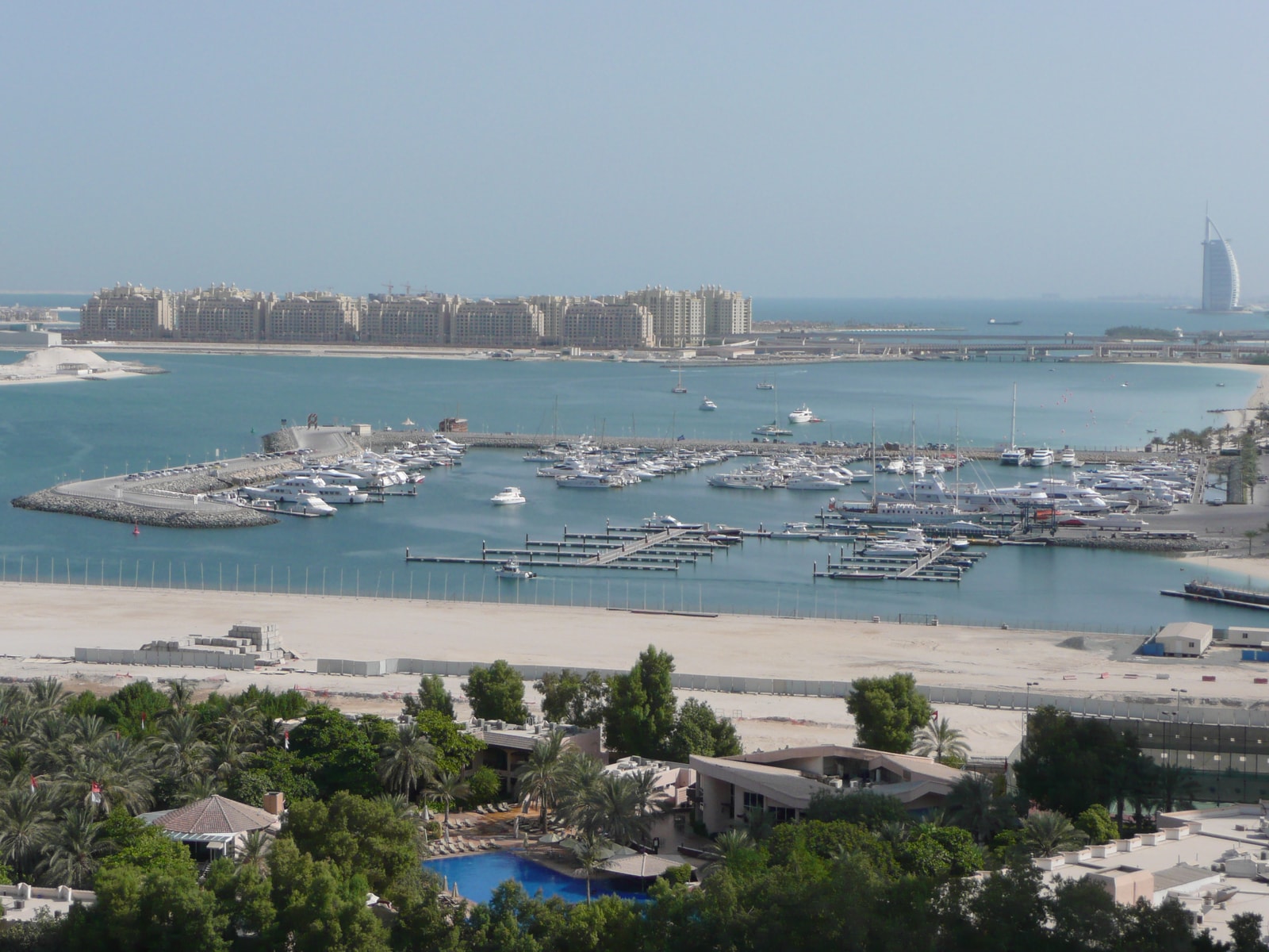 A view from a resort showing the beach, boats in the marina, and the towering Dubai skyline in the distance.