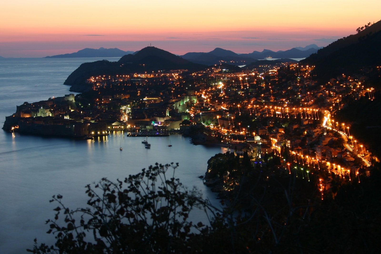 The harbor in Dubrovnik illuminated at twilight, with lights reflecting on the water.