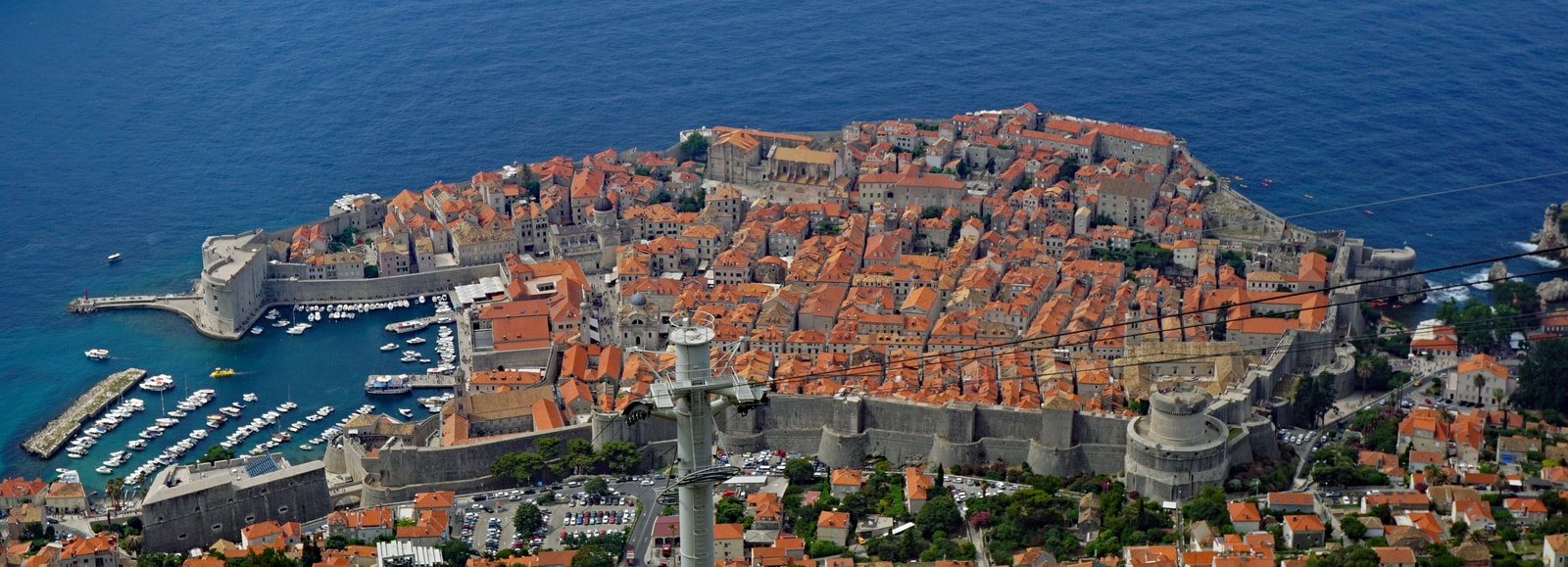 A wide panoramic view of Dubrovnik's Old Town, harbor, and the surrounding Adriatic Sea.