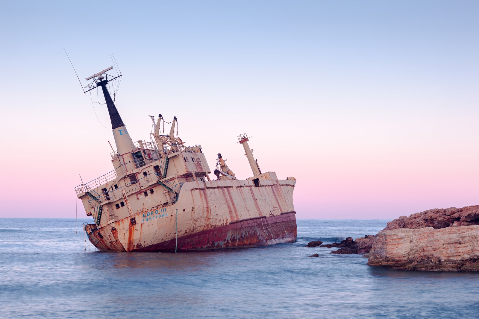 A close view of the Edro III shipwreck in its rocky setting during twilight.