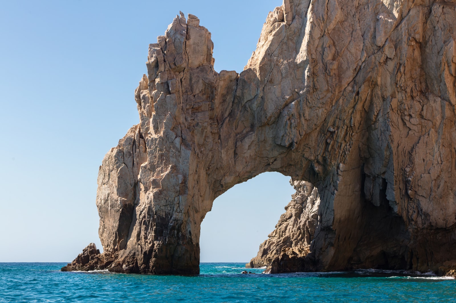 A close-up view of the iconic El Arco rock formation at Land's End in Cabo San Lucas, with turquoise water swirling around its base.