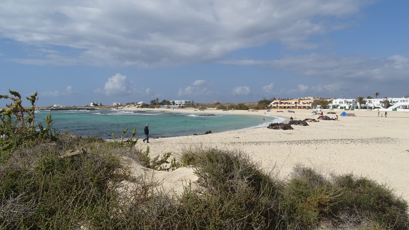 A wide view of a bay at El Cotillo, showing the town, the harbor, and the beach under a cloudy sky.