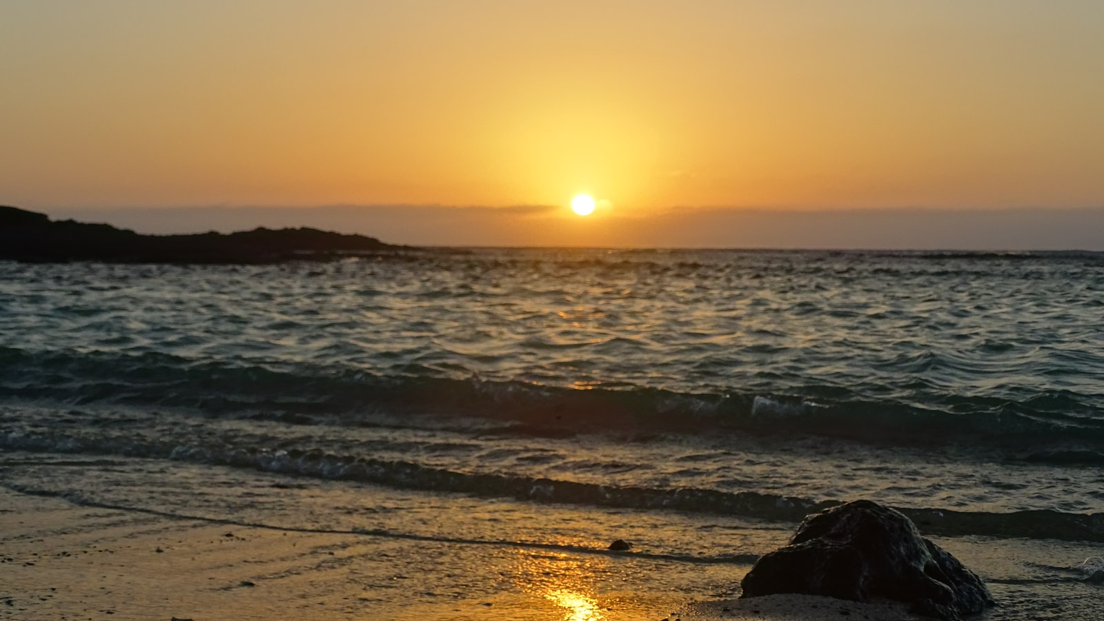 The setting sun casts a golden glow over the wet sands and volcanic rock pools of El Cotillo's coastline.