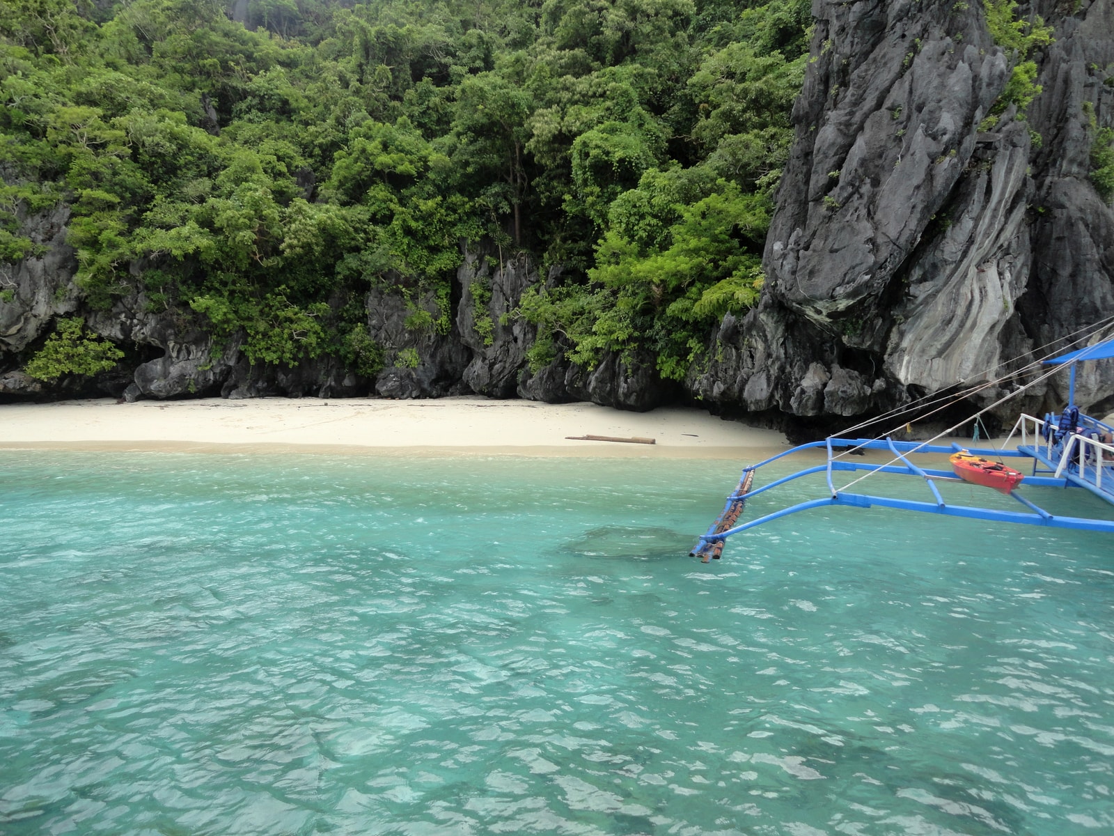 A small outrigger boat floats in a secluded cove with calm, clear turquoise water surrounded by towering limestone cliffs.
