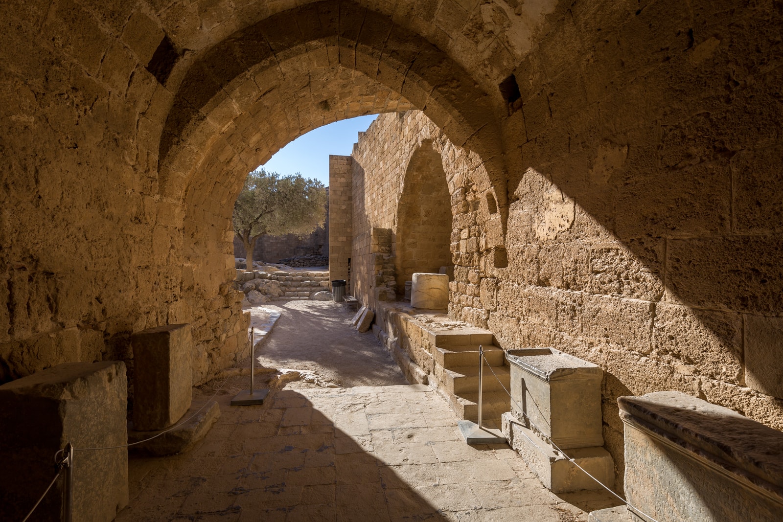 A stone archway frames the sunlit entrance passage to the Acropolis of Lindos.