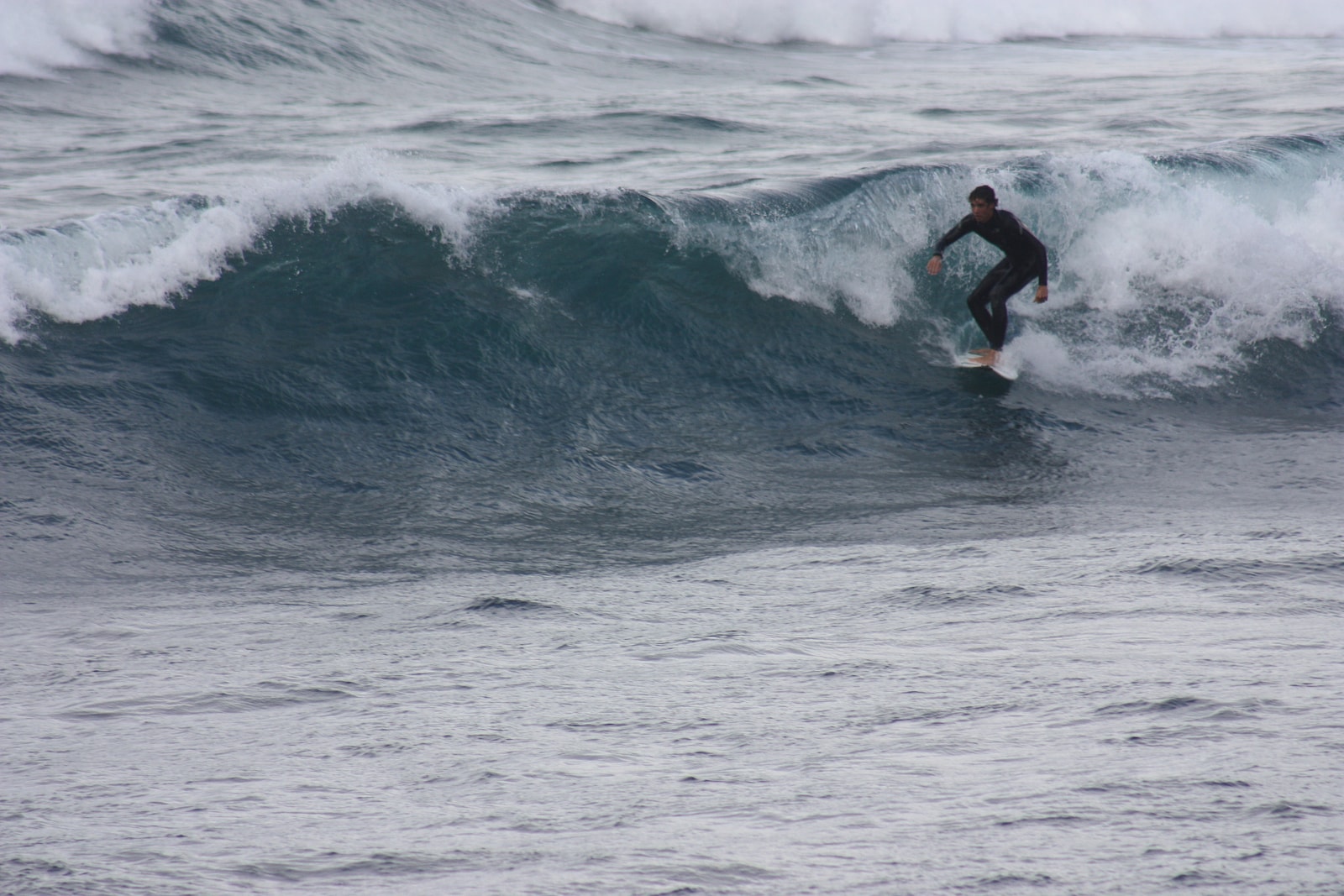 A surfer rides a cresting wave with the dramatic cliffs of Famara in the background.