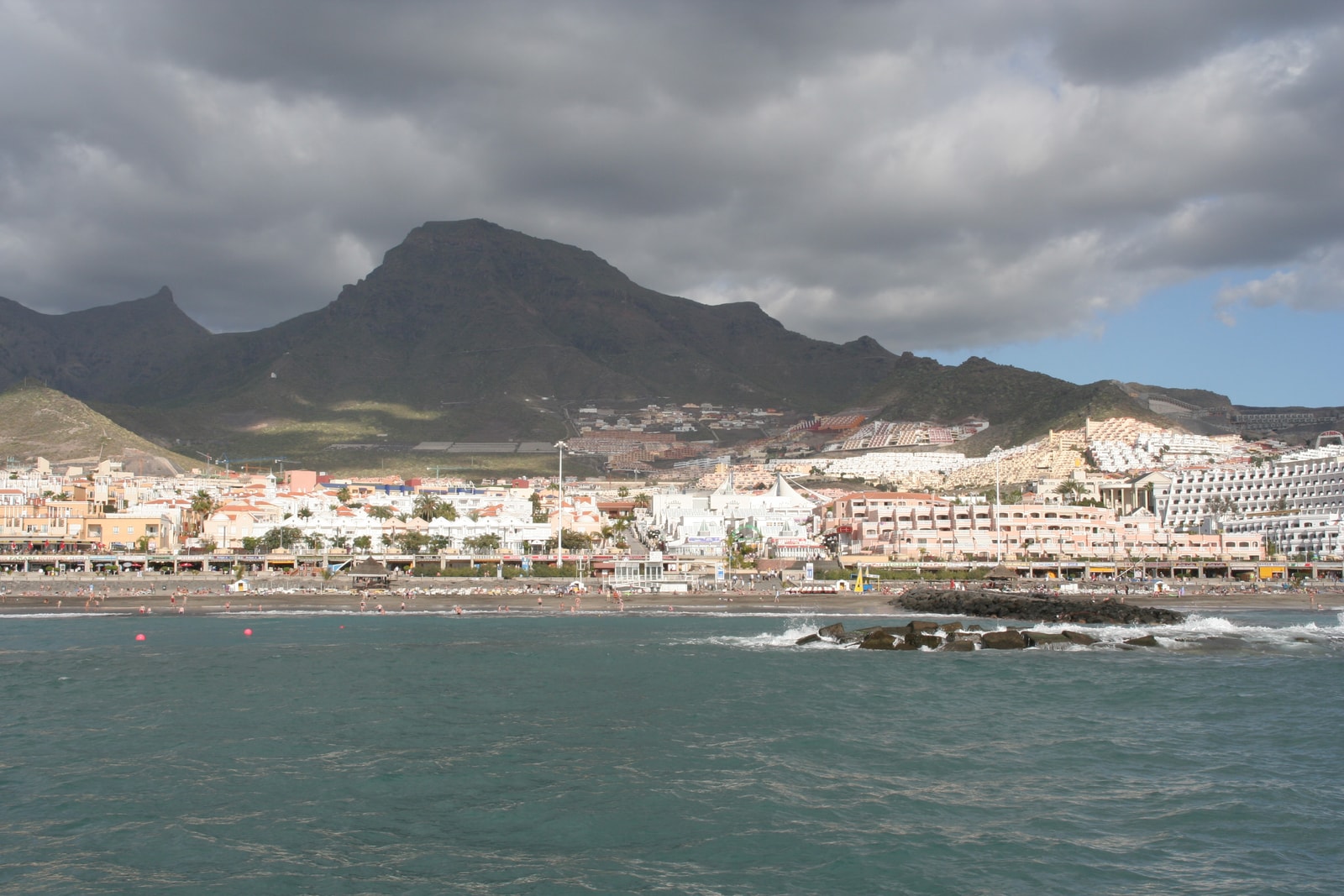 A view of Fañabé beach from a boat offshore, with hotels and mountains in the background.