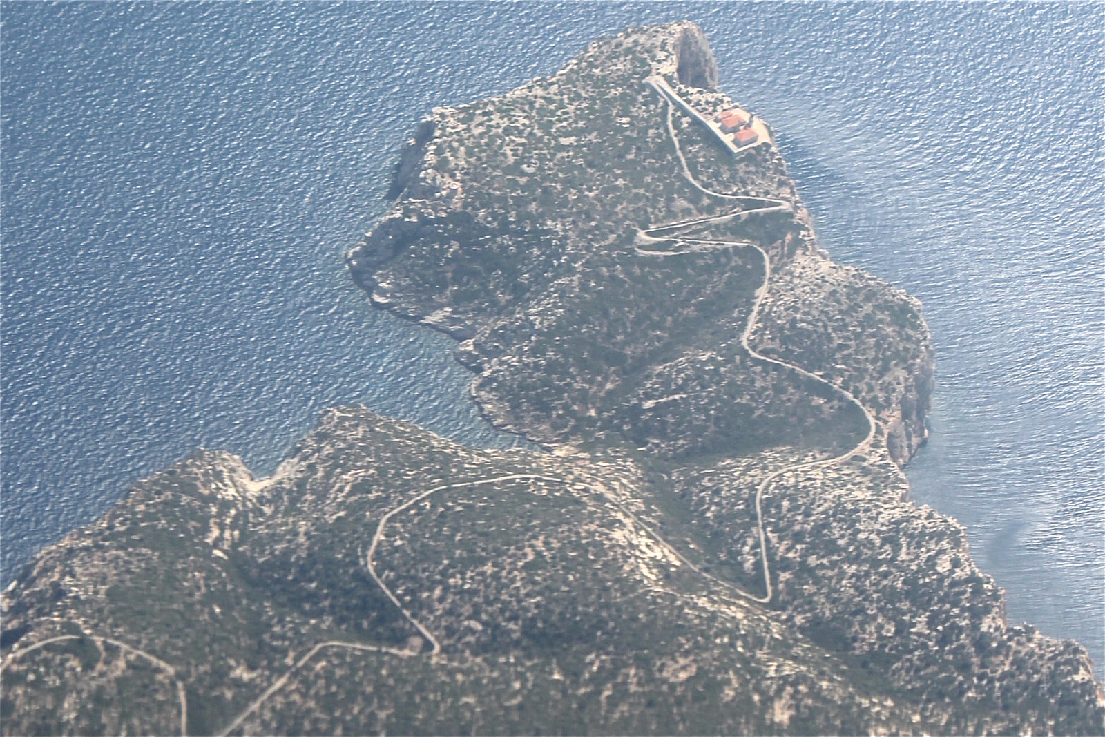 An aerial view shows a long, narrow peninsula with winding roads, surrounded by blue water.