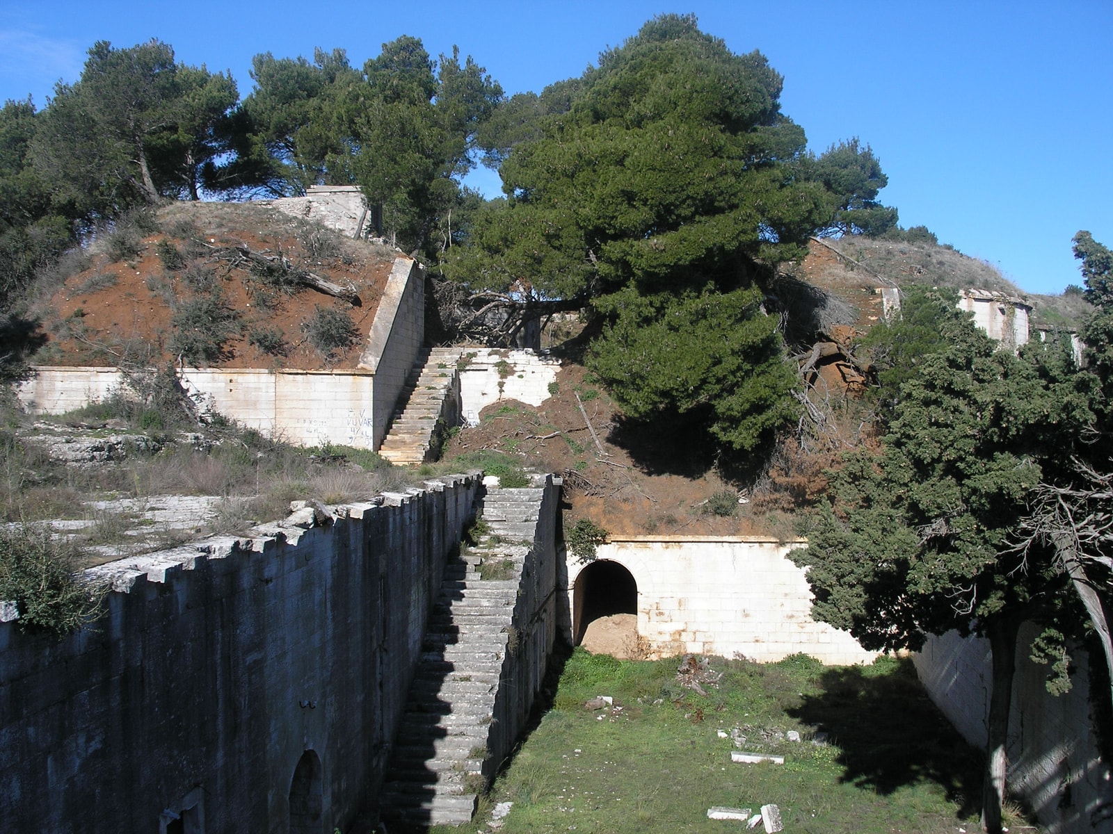 The weathered stone walls and courtyard of Fort Punta Christo, a 19th-century Austro-Hungarian fortress surrounded by pine trees in Štinjan.