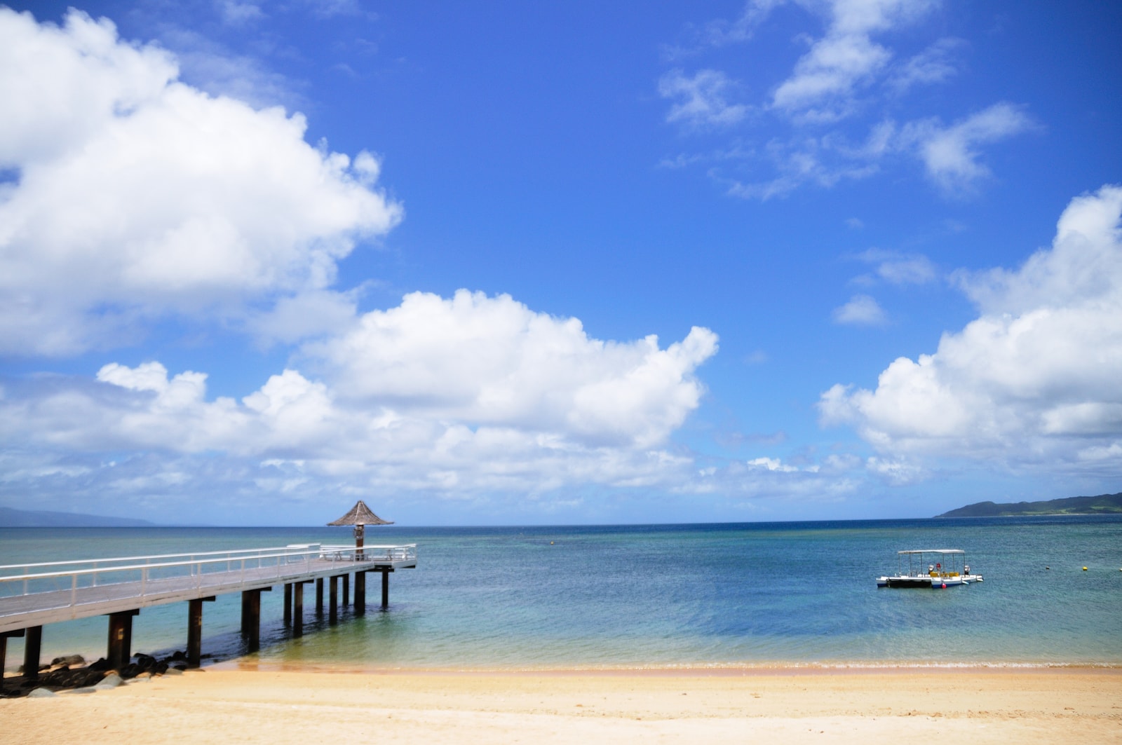 A long, curved beach with a pier extending into the calm, blue water.