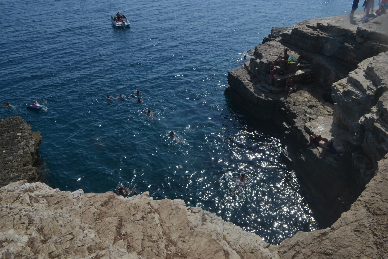 Swimmers float in the deep, glittering water of a cove at Seagull's Rocks, surrounded by stark white limestone cliffs used for diving.