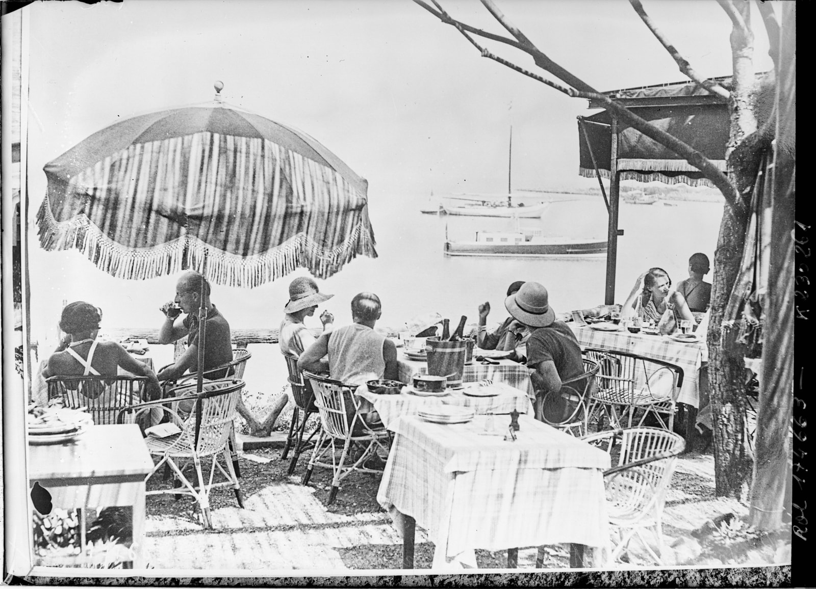A vintage black and white photograph from 1933 shows people dining and relaxing on the sand at Garoupe Beach.