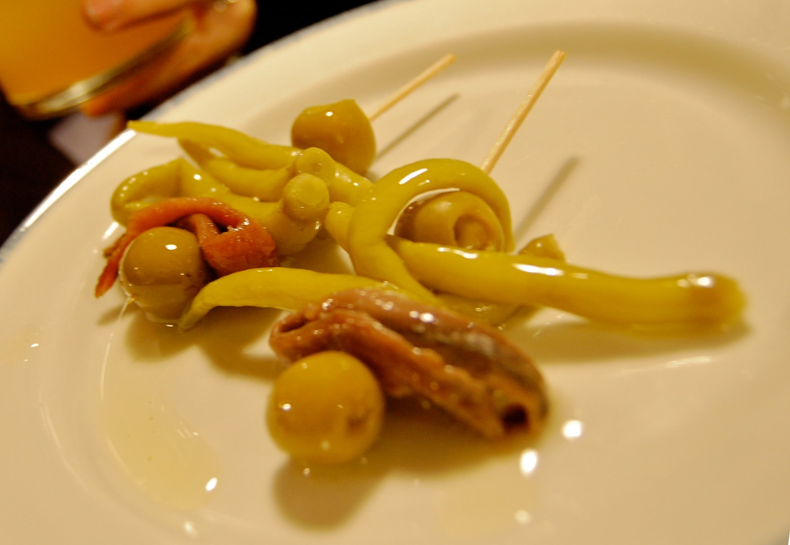 A close-up shot of several 'Gilda' pintxos, each consisting of a pickled green pepper, an olive, and an anchovy skewered on a toothpick.