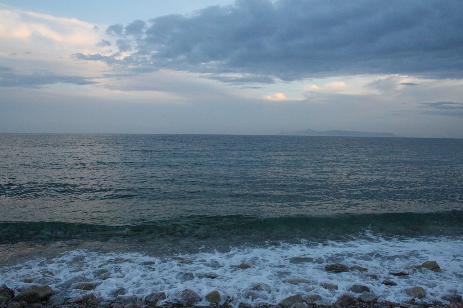 A calm sea at dusk with gentle waves lapping a sandy shore in Glyfada.