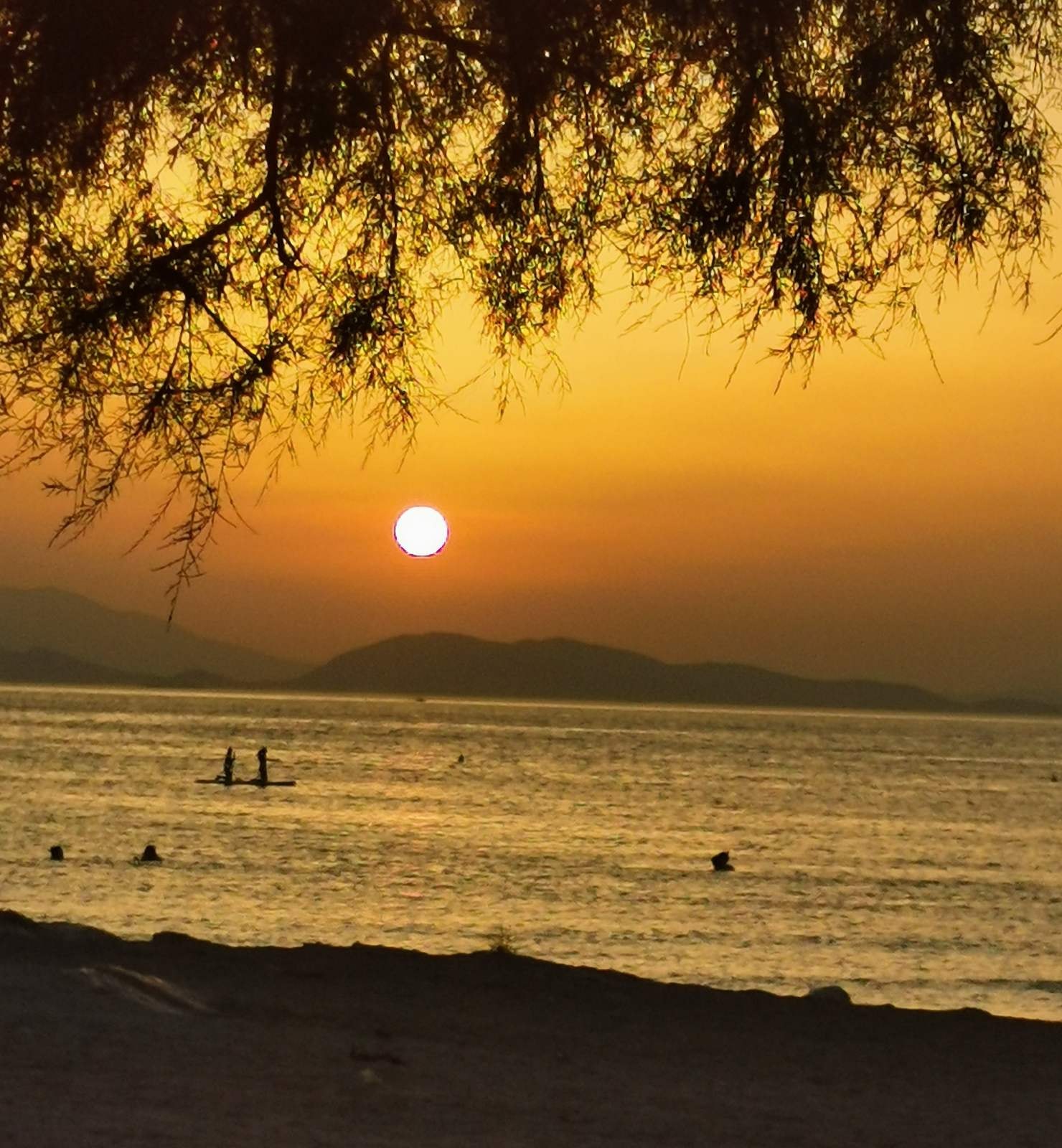 A wide-angle sunset shot showing silhouetted hills and golden light reflecting on the sea in Glyfada.