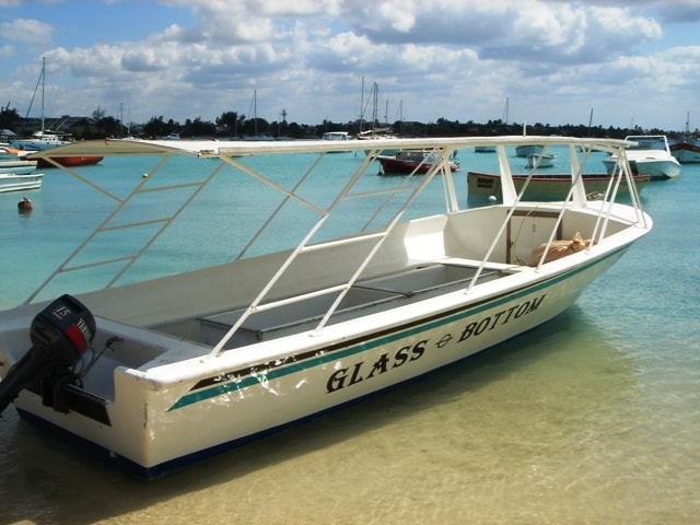 A yellow and white glass-bottom boat named 'Le Surcouf' floats on the turquoise water in Grand Baie.