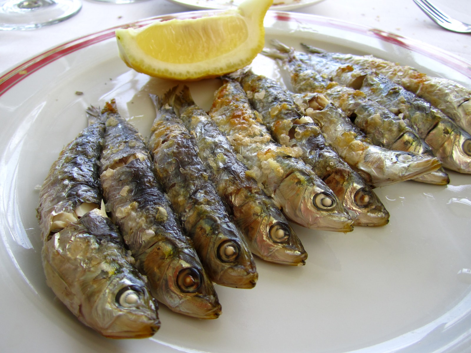 A close-up of perfectly grilled espeto de sardines seasoned with sea salt, served on a plate at a beachside chiringuito.