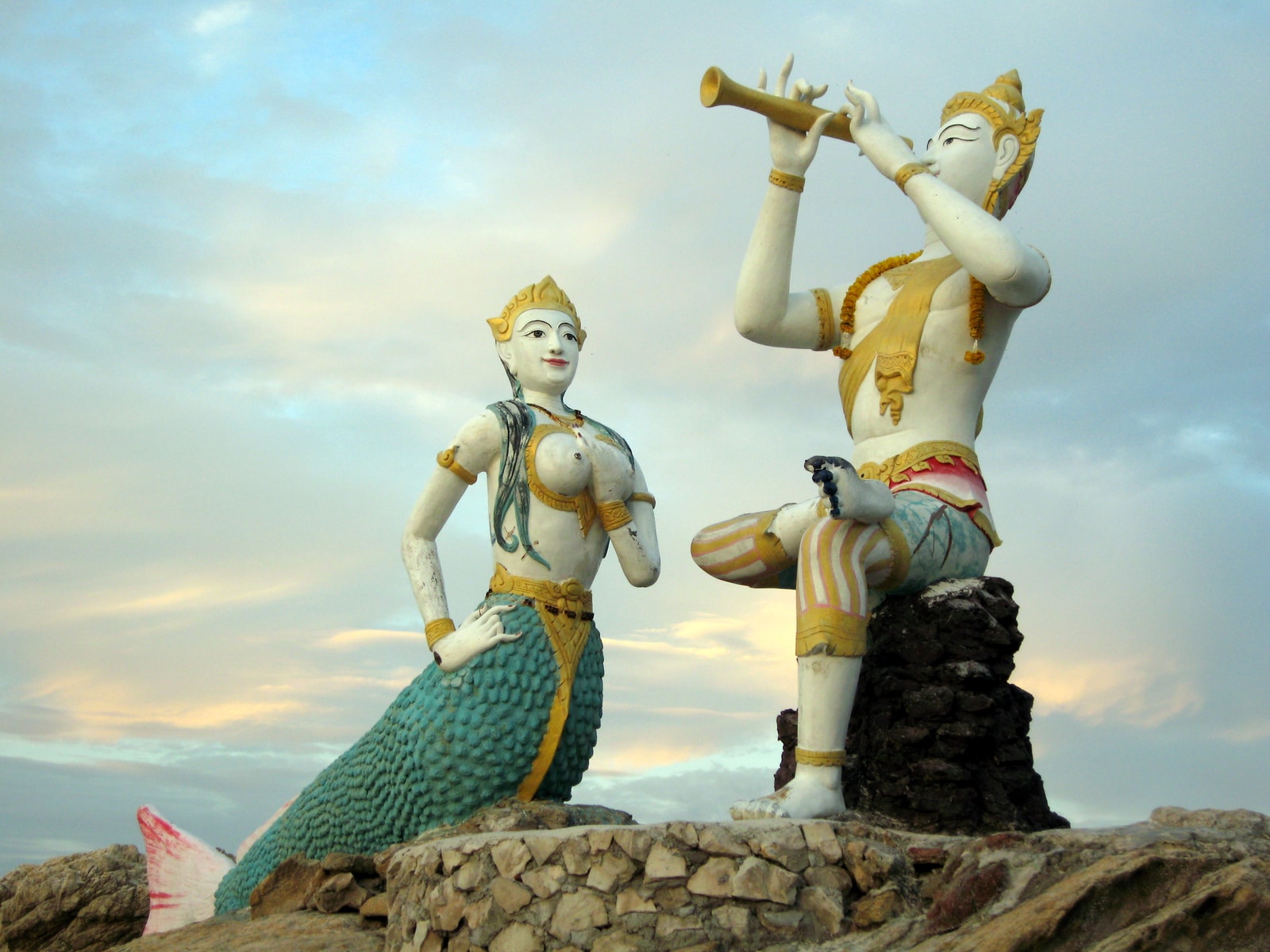 A distinctive mermaid statue on the rocks at Hat Sai Kaew on Koh Samet during a colorful sunrise.