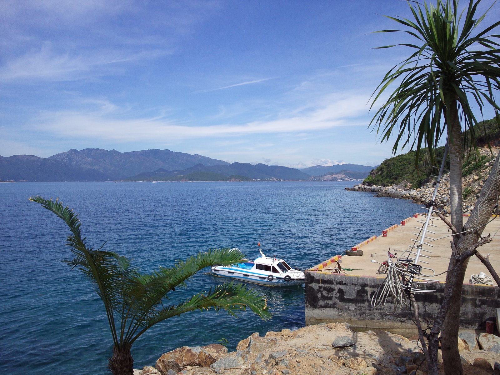 A view of the Hon Tre coastline showing a pier, a boat in the water, and green mountains in the distance.