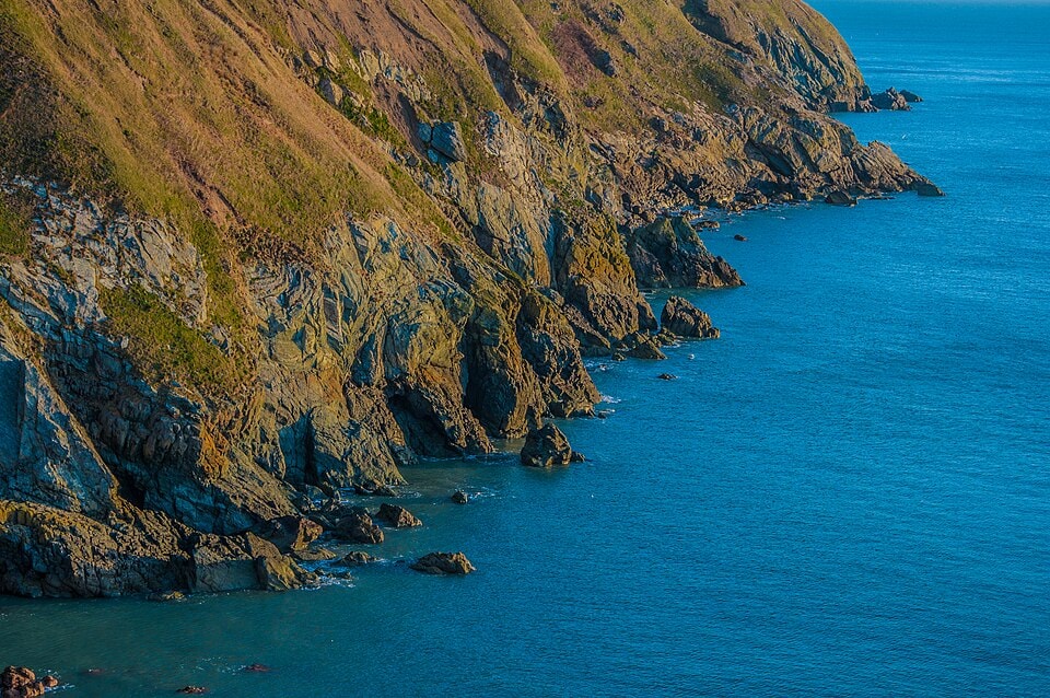 Rugged cliffs with patches of green vegetation drop down to a vibrant blue sea.