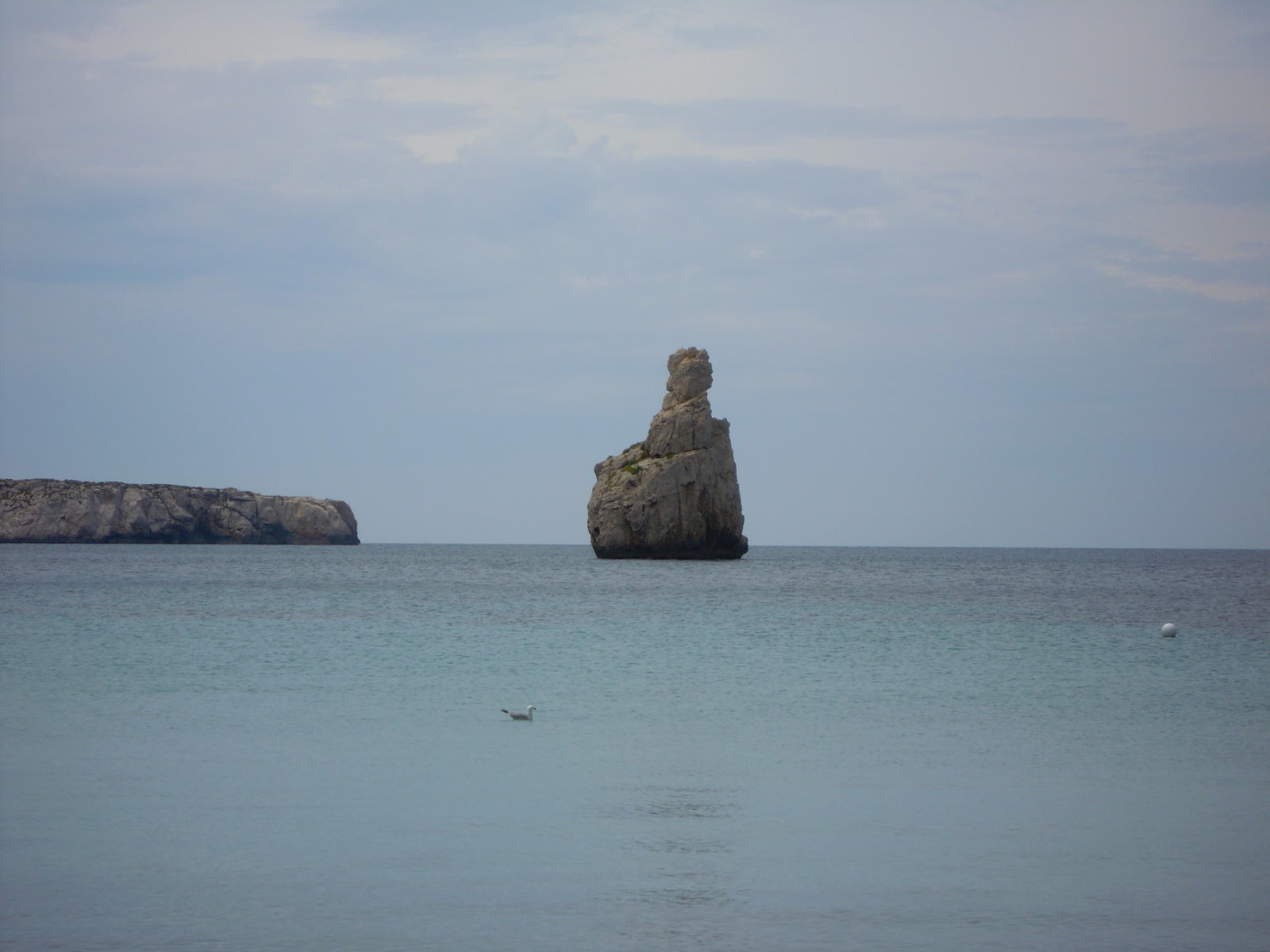 A view of the iconic Cap Bernat rock formation rising from the sea in the middle of Benirràs bay, a hallmark of Ibiza's rugged northern coast.